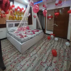 A 'Just Married' room decoration featuring a canopy with lights, 'I ❤️ U' spelled out in rose petals on the bed, and red and white balloons.