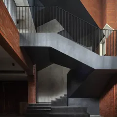 The central staircase in the Brick House is a sculptural element crafted from black pigmented lime plaster. It winds through the home, its sharp, geometric forms creating a dramatic contrast with the warm texture of the surrounding brick walls.