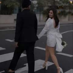 A classic "follow me" pose with a twist. As they cross the street, she looks back with a smile, inviting him and the viewer into their shared journey. The focus on the back of her dress with its elegant bow adds a lovely detail.