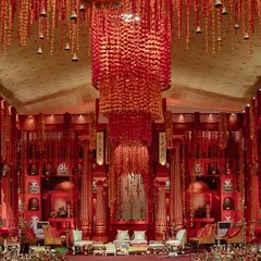 A wide view of the 'Lal Bagh' mandap, showing the scale of the temple-inspired design. The massive, handcrafted shola flower chandelier creates a central focal point, drawing the eye and adding to the grandeur of the ceremony.