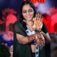 A smiling bride proudly showing her intricate portrait mehandi.
