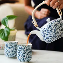 A woman pours chai from a beautiful blue and white ceramic teapot into matching cups. This action shot brings the product to life, creating a warm and inviting moment that resonates with tea lovers.