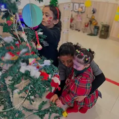 An instructor helps a toddler decorate the Christmas tree, a wonderful collaborative activity that brings everyone into the holiday spirit.