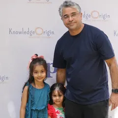 A father and his two daughters pose in front of our "Knowledge Origin" backdrop during a school event.