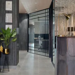 A view of the office corridor, showcasing the material palette of black ash wood, grey floor tiles, and terrazzo. The glass pivot door provides a glimpse into the workspace, maintaining a sense of transparency.