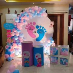 A classic "Boy or Girl" themed baby shower decoration for a home setting. The setup features a circular backdrop with pink and blue footprints, a balloon arch, and "BABY" blocks for a gender reveal party.