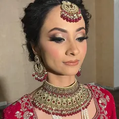 A classic bridal glam look featuring soft, shimmering eyeshadow and defined lashes. The intricate updo and traditional red jewelry complete this elegant wedding day style.