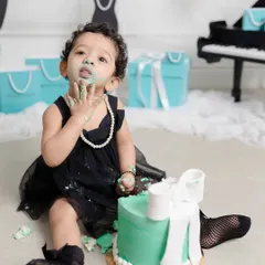 A "Breakfast at Tiffany's" themed cake smash, where this little lady is enjoying her cake with pearls and style. It's a perfect example of a chic and fun first birthday shoot.