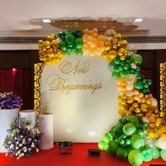 A sophisticated backdrop for an engagement party or roka ceremony. This setup features a 'New Beginnings' message on a white circular board, framed by an organic balloon arch in shades of green and gold.