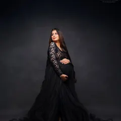 A full-length portrait in a dramatic black lace and tulle gown. This shot highlights the elegant silhouette of the mother-to-be against a classic dark backdrop.