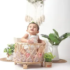 This baby's joyful, upward glance is simply infectious. Captured during a sitter session, this portrait uses a boho-chic setup with natural textures and greenery to create a warm and inviting atmosphere.