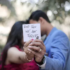 The couple holds up a handwritten note to announce their growing family. This type of prop-focused shot is perfect for sharing on social media.
