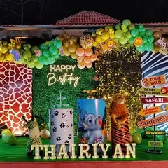 I bring the jungle to your party with this exciting safari-themed birthday decoration. The setup includes a lush green backdrop, animal print panels, an organic balloon arch in jungle colors, and fun props like animal figures and road signs to create an immersive adventure for a first birthday.
