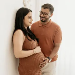 A candid moment of connection between the expecting couple. The warm, earthy tones of their outfits complement the natural, boho-inspired studio setup.