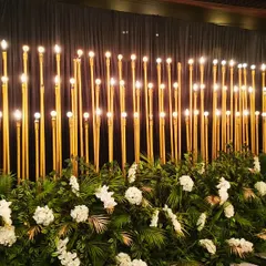 A dramatic and glamorous photo wall for a cocktail night. The backdrop features a forest of tall, slender gold lamps against black drapes, creating a warm, ambient glow perfect for evening photos.