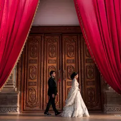A new beginning. This wide shot captures the couple walking past magnificent carved doors and dramatic red curtains, creating a sense of grandeur and anticipation.