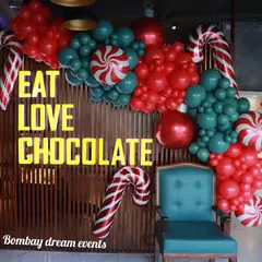 This Christmas selfie corner I designed for a chocolate shop features a fun balloon arrangement with candy cane props against a wooden wall, perfectly matching the 'Eat Love Chocolate' theme.