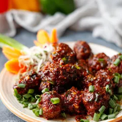 A close-up of saucy Veg Manchurian, a popular Indo-Chinese dish, garnished with fresh spring onions.
