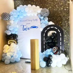 A sleek and modern car-themed second birthday. The "Two Fast" theme is brought to life with a custom white backdrop, a balloon arch in blue, black, and white, and a fun racetrack cutout.