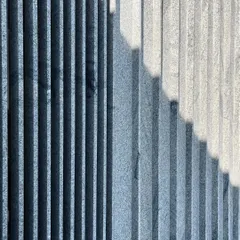 The texture of stone and the rhythm of shadows. This is a close-up of a fluted stone facade, where the changing angle of the sun creates a constantly evolving pattern of light and dark.