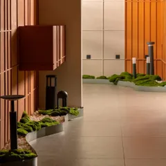 For this lighting showroom, the goal was to let the products shine. We created a clean, gallery-like space using a neutral palette, then introduced organic elements like this curved moss bed and bold terracotta paneling to guide the eye and add warmth.