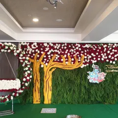 This is a full view of a Krishna-themed naming ceremony. I created a dense backdrop of foliage to represent a forest, complete with a custom tree cutout, a floral arch for the cradle, and a prominent illustration of Krishna to bring the theme to life.