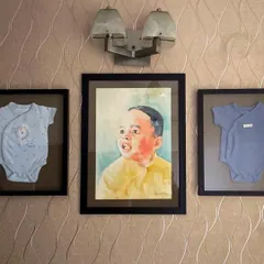 The final display of the child's portrait, beautifully framed between his first onesies. This is a wonderful example of how to turn a commissioned painting into a deeply personal piece of family history.