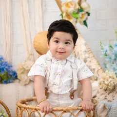 A close-up of a handsome little man in a boho-inspired setting. The soft textures of the wicker basket and surrounding flowers create a gentle and natural portrait.
