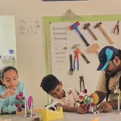 An instructor helps two students assemble their water turbine models. This project involves metal parts, gears, and a simple generator.
