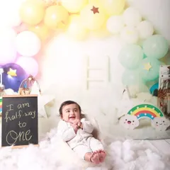 "I am halfway to one." This cheerful half-birthday session uses a rainbow and clouds theme to celebrate the six-month milestone. The baby's delighted expression shows just how much fun we have in the studio.