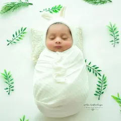 A cute bunny bonnet for this little one, who is swaddled and lying on a tiny pillow, surrounded by scattered leaves for a whimsical touch.