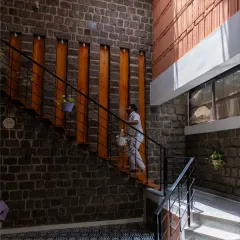 The floating staircase against a rugged stone wall is a central feature in the Gifty Residence. The contrast between the dark stone and the warm wood of the steps creates a dramatic and beautiful focal point.
