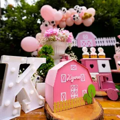 Custom props bring the theme to life. This personalized pink barn and light-up initial 'K' create a beautiful focal point on the dessert table, making the celebration feel truly special and unique.