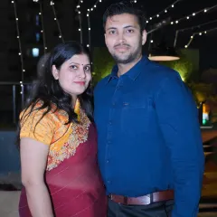 A couple poses for a photo at an evening event with beautiful string lights in the background.