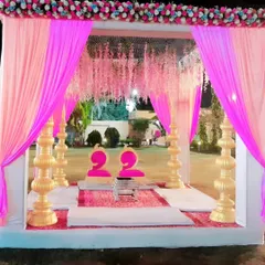 A beautiful pink and white themed mandap for an evening wedding. The structure is decorated with pink drapes, hanging floral strings, and ornate golden pillars.