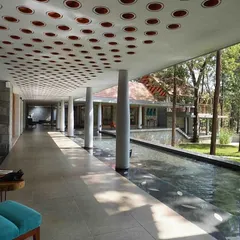 In this hospitality project, a long, open corridor runs alongside a tranquil water channel. The design, featuring a perforated ceiling and natural materials, creates a sensory journey that connects visitors to the surrounding coffee estate.