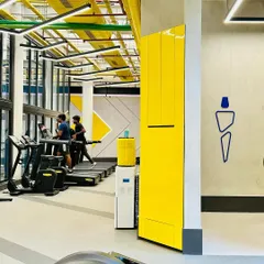 The cardio section of the DLF Thrive Gym in Chennai. The space is designed with an industrial aesthetic, featuring exposed ceilings and services painted in bright yellow, creating a high-energy environment for workouts.