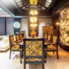 A head-on view of the dining setup, highlighting the symmetry and richness of the design. The chairs, upholstered in a classic Versace print, are paired with a custom-designed ceiling and a tiered antique brass chandelier, creating a truly regal atmosphere.