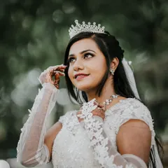 A beautiful close-up of a Christian bride looking up, her portrait framed by lush green foliage. The soft lighting highlights her delicate tiara and lace gloves.