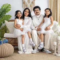 A classic family portrait with everyone looking at the camera. The coordinated white outfits and the bright, airy setting create a fresh and timeless look for this family of four.