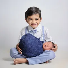 A dapper big brother, complete with a bow tie and suspenders, proudly holds his newborn sibling. This is a classic, heartwarming pose that families adore.