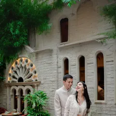 A sweet, candid moment between a couple in front of a beautiful stone building with gothic-style windows. Their joyful interaction contrasts beautifully with the classic architecture.
