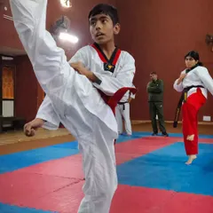 A young student practices a high section kick with precision and focus. Behind him, other students continue their training, showing the disciplined environment of my dojo.