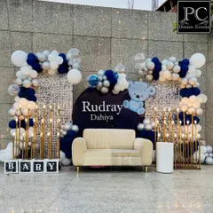 For Baby Rudray's Kuan Poojan ceremony, we designed this chic and modern backdrop. A shimmering silver sequin wall is framed by stylish blue, white, and silver balloon arches, complete with a cozy couch for photos and marquee 'BABY' blocks.