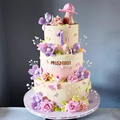 For a magical first birthday, I designed this three-tiered enchanted garden cake. It's adorned with a cascade of hand-sculpted sugar flowers in soft pastel shades, delicate edible butterflies, and a whimsical mushroom house topper. This non-fondant cake shows how elegant and detailed a buttercream finish can be.