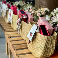 A row of beautiful straw bags, each filled with goodies for the bridesmaids. The custom "Will you be my Bridesmaid?" card with a tassel is the perfect finishing touch.