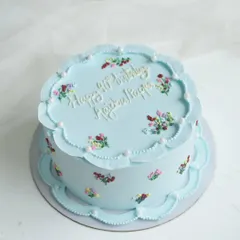 A special cake for a 90th birthday, designed with vintage charm. This light blue cake features delicate, hand-piped floral details and a scalloped border, honoring a life full of wisdom and love.