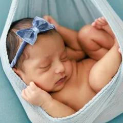 Gently cradled in a soft blue sling, this newborn is in a classic and safe "womb" pose. The monochromatic color scheme creates a calm and soothing visual, highlighting the baby's peaceful slumber.