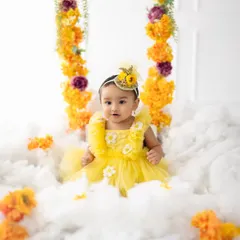 A dreamy first birthday setup with a baby girl in a yellow dress, sitting on a cloud with a floral swing. We create magical sets to make their first birthday unforgettable.
