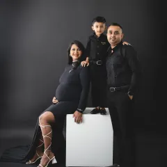A powerful family portrait in matching black outfits. The son stands proudly on a block, showing off his new status as a big brother in this dramatic studio shot.